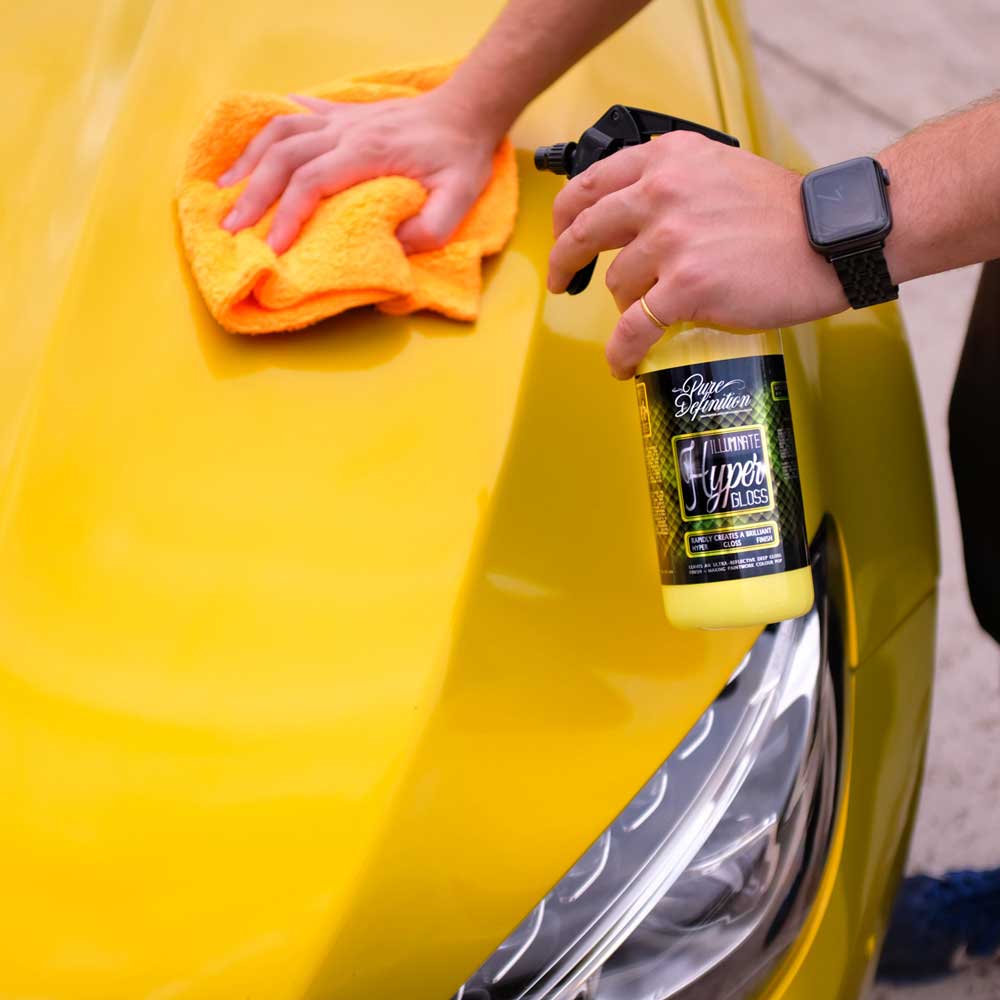 spraying and wiping illuminate hyper gloss on a yellow cars bonnet with a cloth.